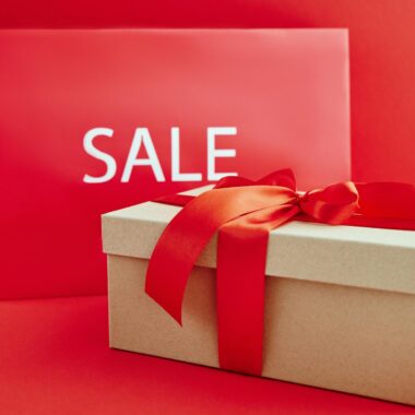 Gift box with red ribbon on red background with sale sign, perfect for retail promotions.