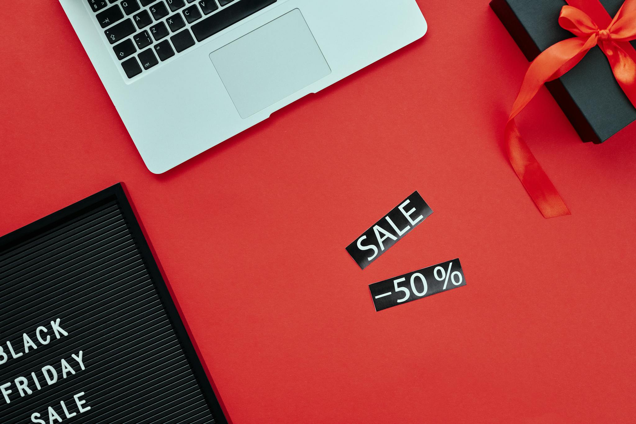 Overhead view of a laptop and gift box on a red surface with Black Friday sale sign.