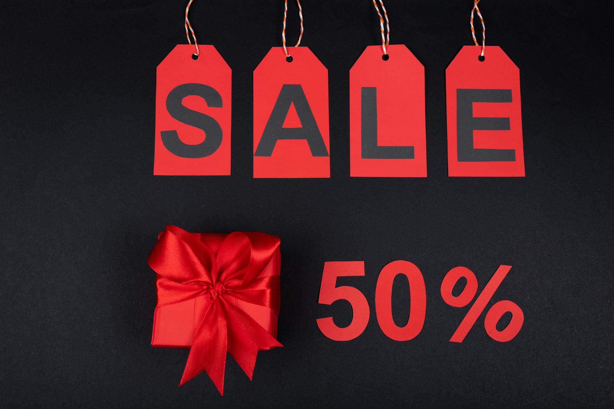 Red gift box next to sale tags and 50% sign on black background, ideal for promotions.